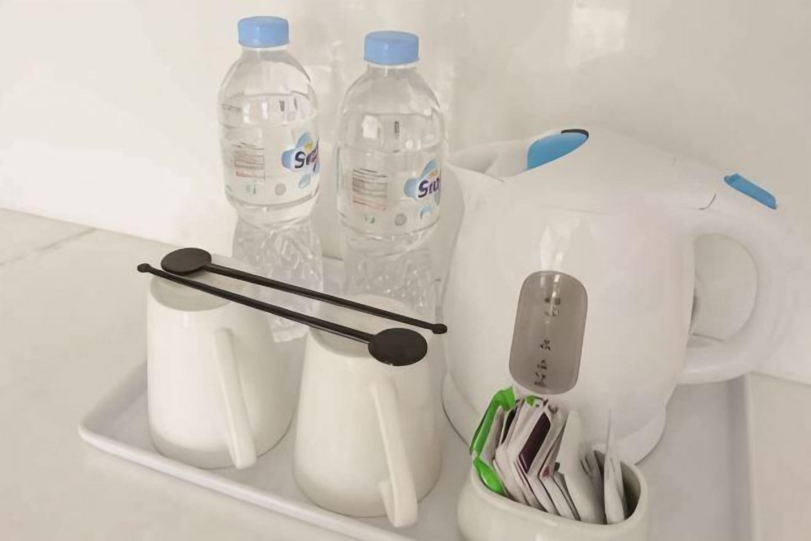 Una zona de cocina con encimera blanca, dos botellas de agua, una tetera blanca y una cafetera.