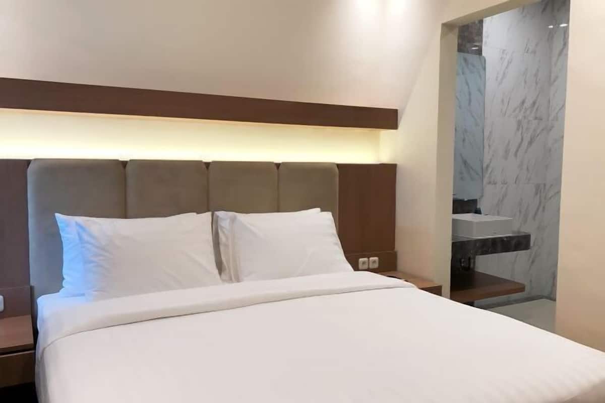 A hotel room with a bed, nightstands, a marble bathroom, and a wooden headboard.