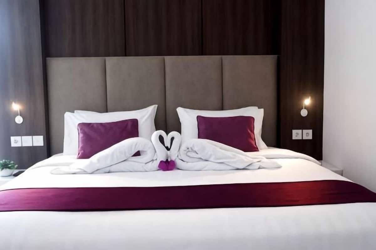 A neatly made bed with a red bedspread, two white pillows, and a decorative towel arrangement.