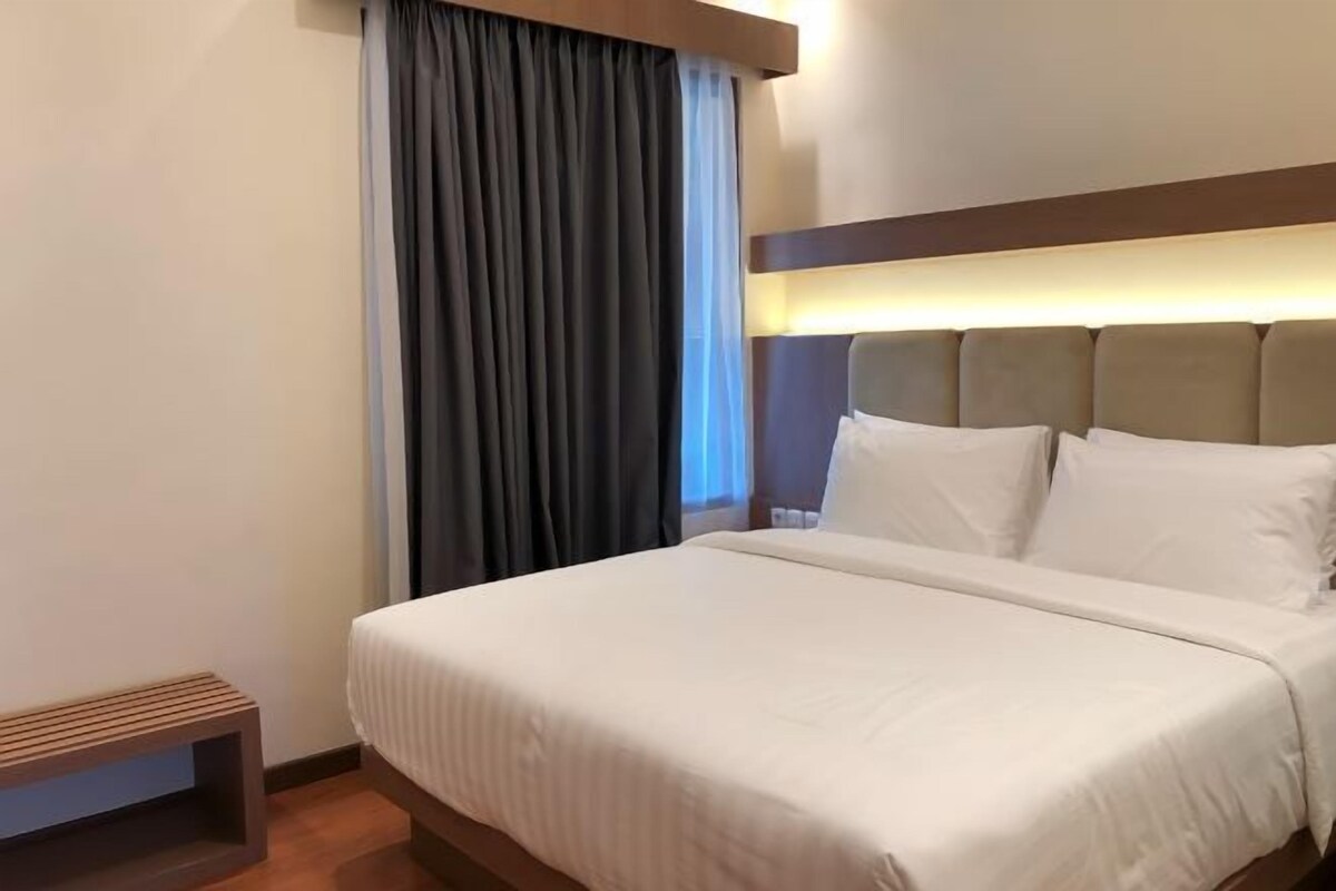 Une chambre d’hôtel avec un lit, une tête de lit, une table de chevet et une fenêtre avec des rideaux.