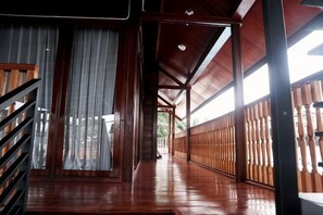 Un pasillo interior de madera con una escalera, barandillas de madera y vistas a través de una ventana.