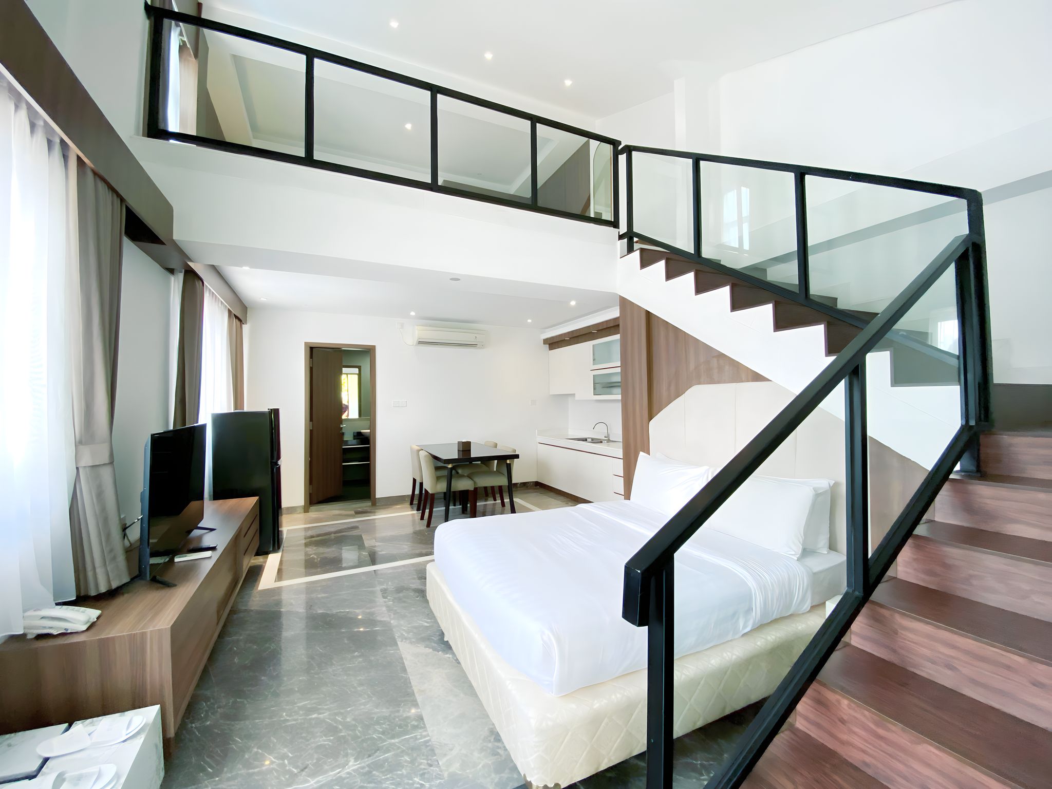 Habitación de hotel moderna con una cama grande, un escritorio, una televisión y una escalera que conecta con un nivel superior.