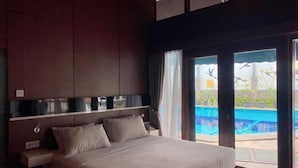 A bedroom with a large bed, a nightstand, and a view of a swimming pool through large windows.