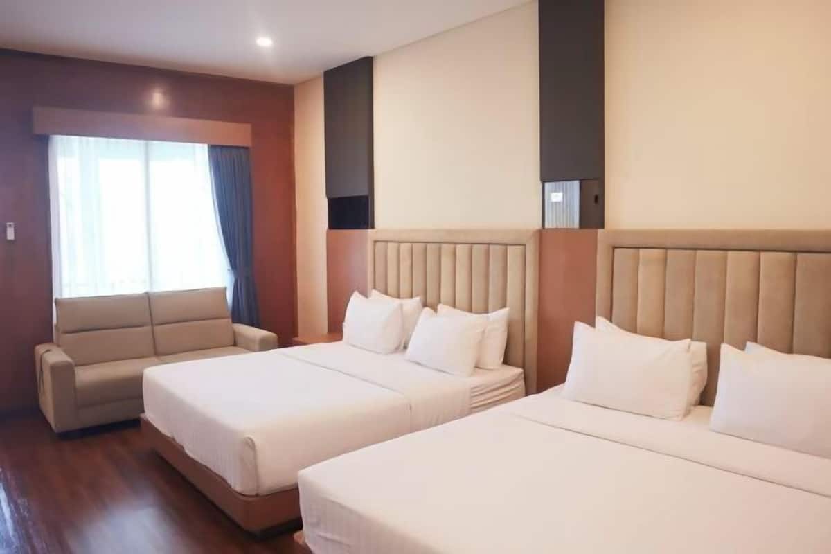 A hotel room with two beds, a sofa, and a large window with curtains.