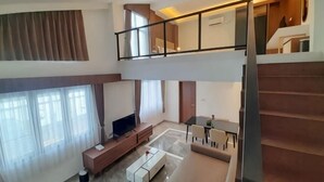 A spacious living area with a high ceiling, a balcony, a staircase, and a flat-screen TV.