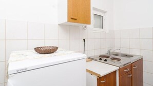 Una cocina compacta con baldosas blancas, un mueble de madera, un ventanal pequeño y un electrodoméstico blanco con una cesta encima.