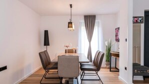 A modern dining area with a rectangular table, four chairs, a pendant light, and a window with curtains.