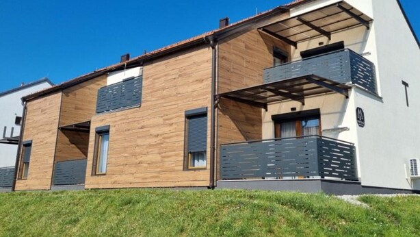 A modern two-story house with a wooden facade and a balcony on the upper floor.