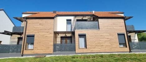 Una casa moderna de dos pisos con techo plano, un balcón visible y un pequeño porche delantero.