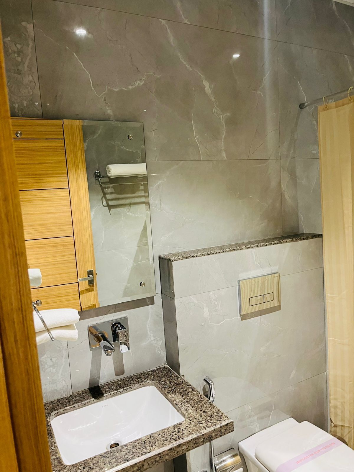 A modern bathroom with a marble sink, wooden cabinet, and a glass shower enclosure.
