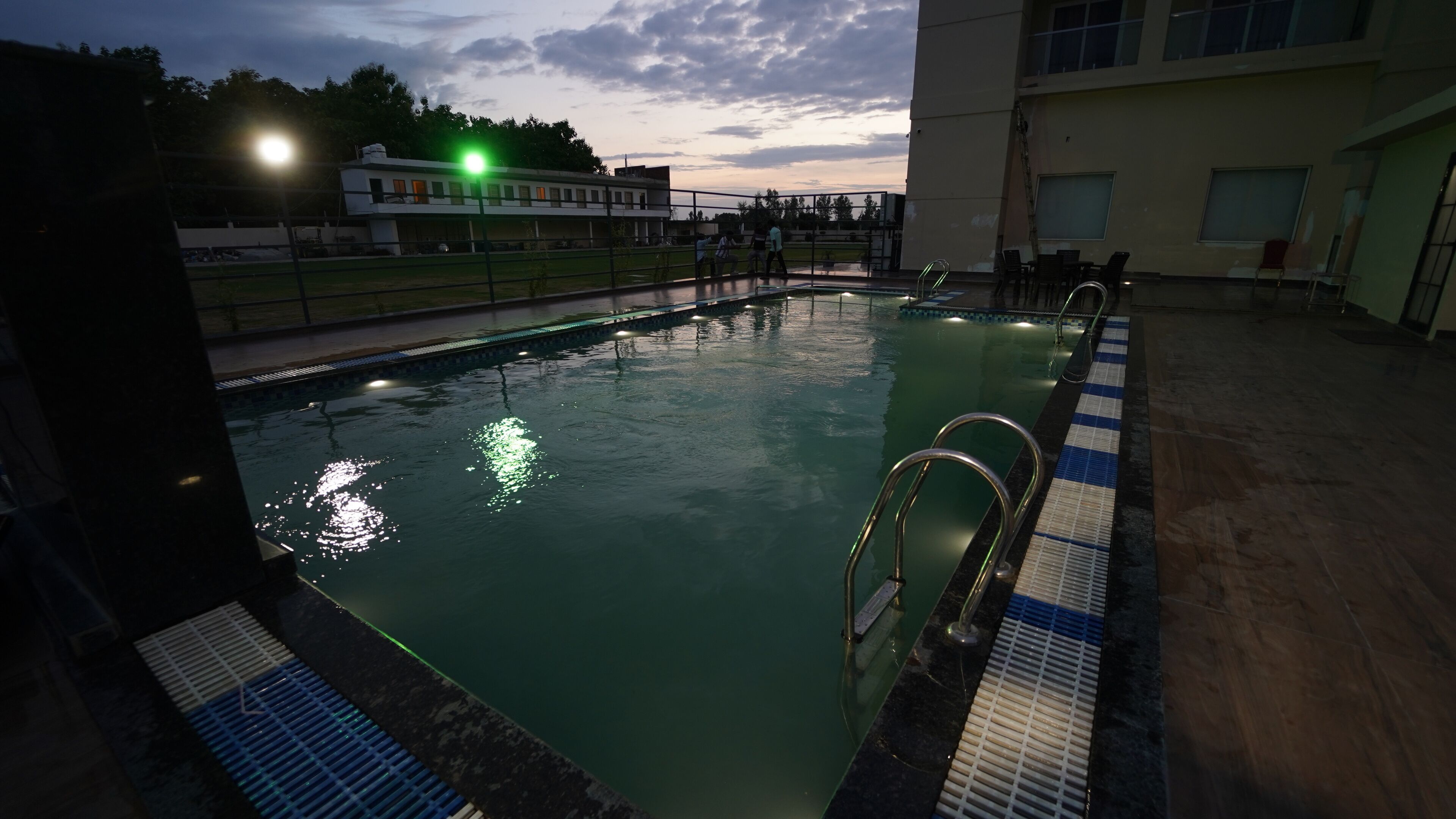 Una piscina con agua cristalina, pasamanos metálicos y un borde con baldosas.