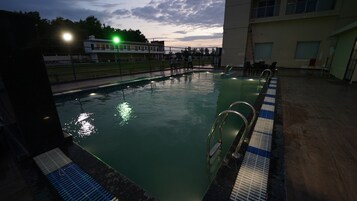 Una piscina con agua cristalina, pasamanos metálicos y un borde con baldosas.