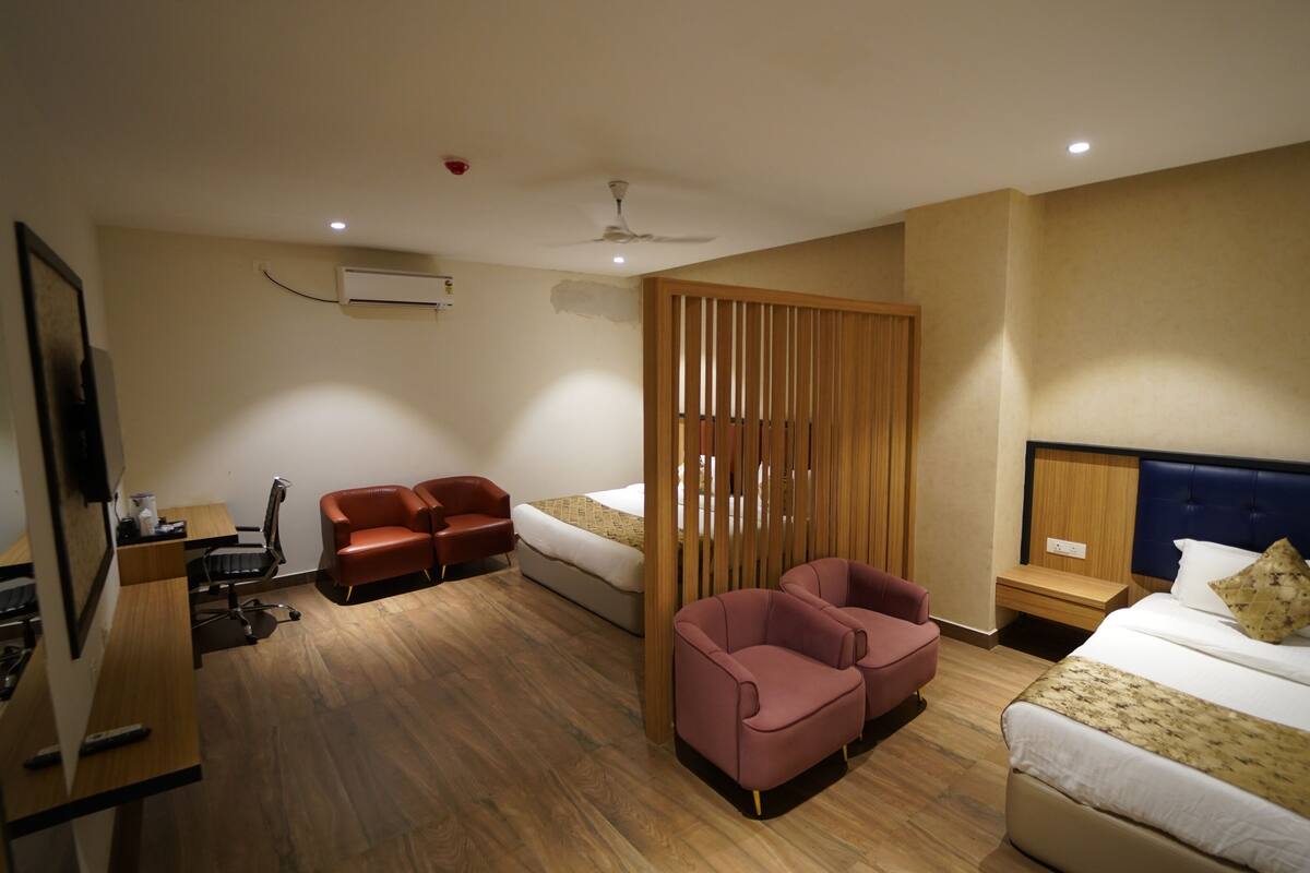 A hotel room with a wooden floor, a bed with a headboard, a desk with a chair, a sofa, a partition, and a ceiling fan.