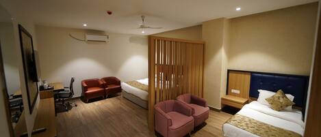 A hotel room with a wooden floor, a bed with a headboard, a desk with a chair, a sofa, a partition, and a ceiling fan.