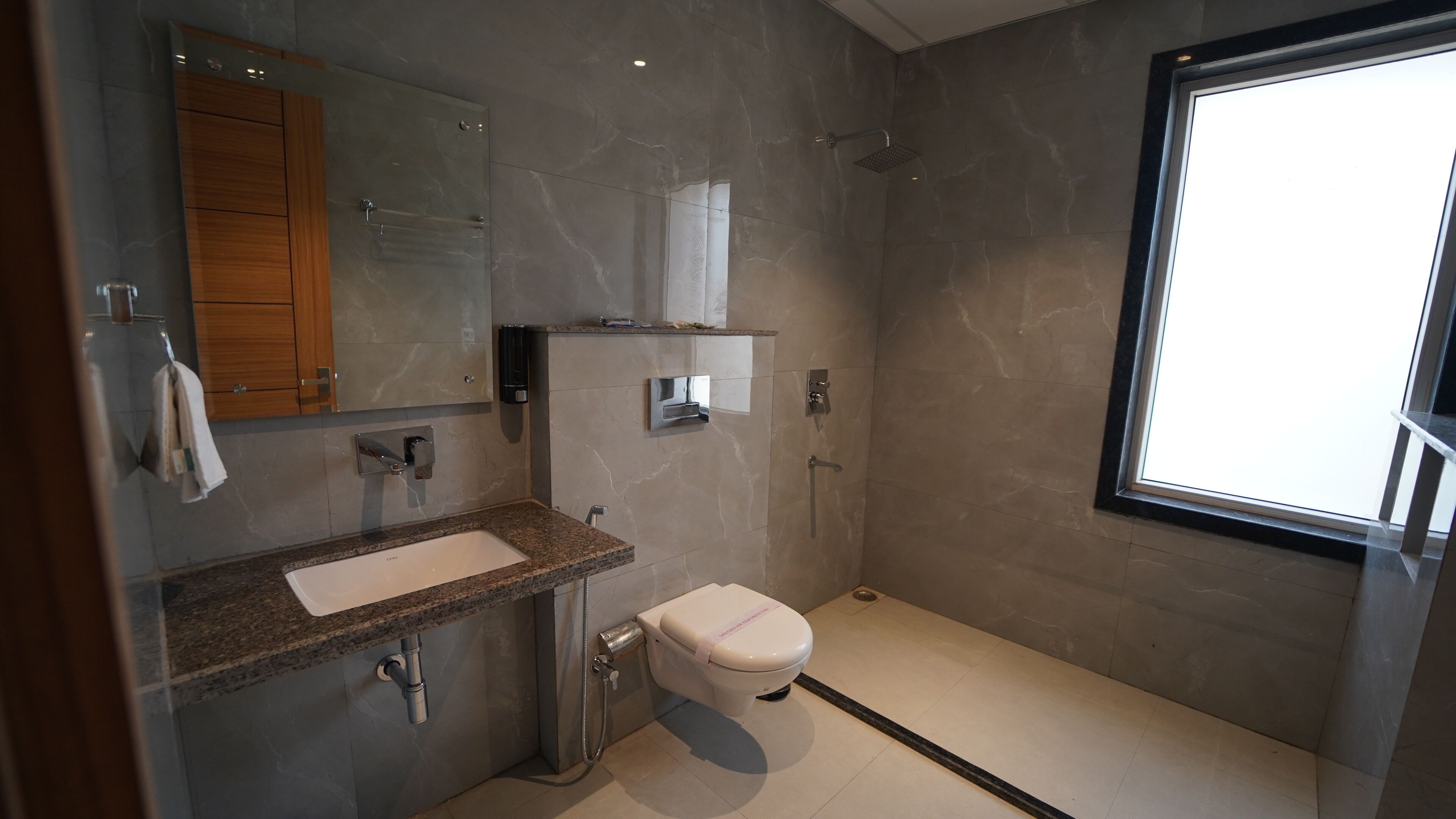 A modern bathroom with a marble wall, a sink with a towel rack, a toilet, and a shower.