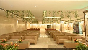 Un hallo amplio con filas de sofás color beige y mesas, decorado con plantas colgantes y arreglos florales.