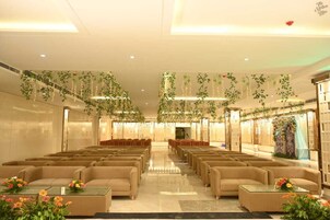 Un hallo amplio con filas de sofás color beige y mesas, decorado con plantas colgantes y arreglos florales.