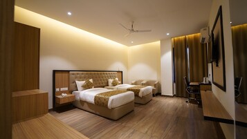 Habitación de hotel con dos camas, un escritorio, una silla, ventilador de techo y televisor montado en la pared.