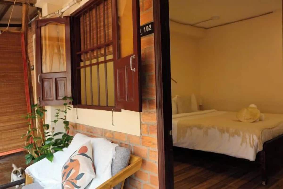 A room with a bed, a wooden bench, and a window with a view of the outside.