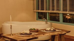 A bathroom with a bathtub, a table with a candle, and a window with blinds. - Canaan Beach Home (Phu Quoc Island)