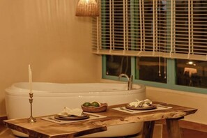 A bathroom with a bathtub, a table with a candle, and a window with blinds. - Canaan Beach Home (Phu Quoc Island)