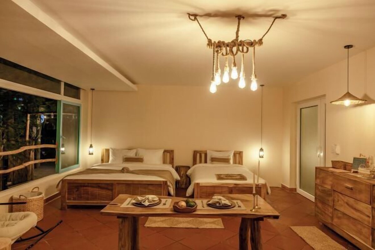 A hotel room with two beds, a dining table with breakfast, a chandelier, and a large window.