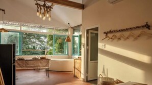 A room with a bed, a table with a chair, a hanging light fixture, and a view through large windows. - Canaan Beach Home (Phu Quoc Island)