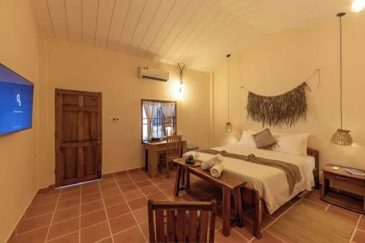 A bedroom with a bed, a desk, a chair, a TV, and a door.