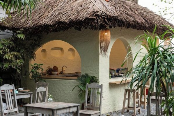 A thatched-roof outdoor dining area with tables and chairs, surrounded by arches and plants. - Canaan Beach Home (Phu Quoc Island)