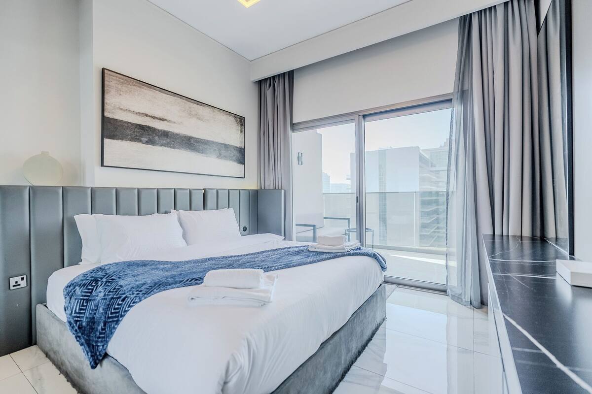 A modern hotel room with a large bed, a view of the city, and a balcony with curtains.