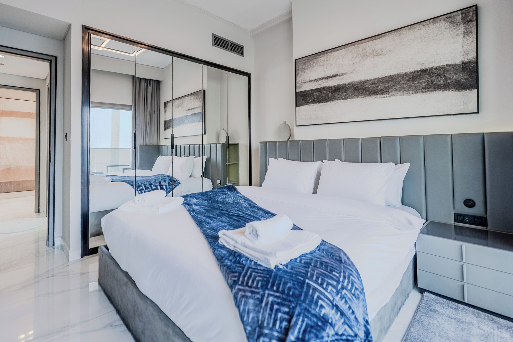 Une chambre d’hôtel moderne avec un grand lit, un miroir, une table de chevet et une œuvre d’art accrochée au mur.