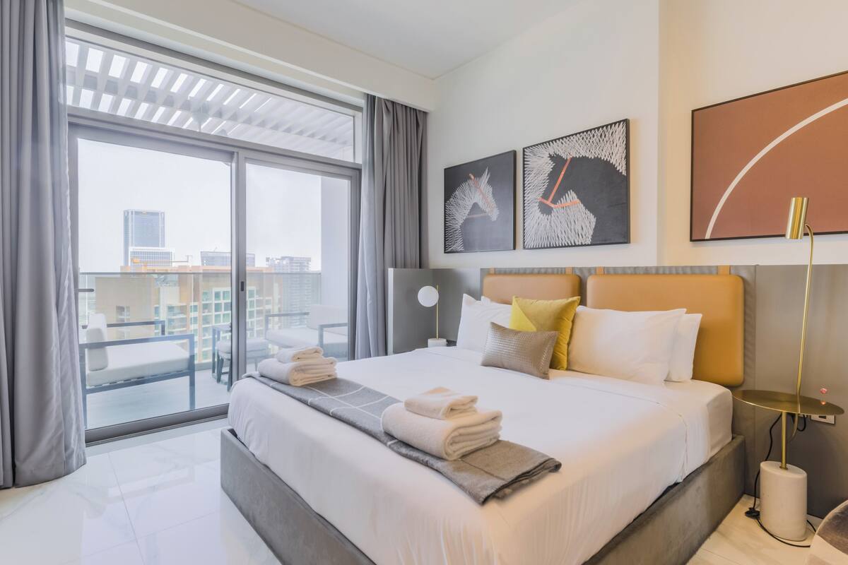 A modern hotel room with a large bed, a view of the city, and artwork on the walls.