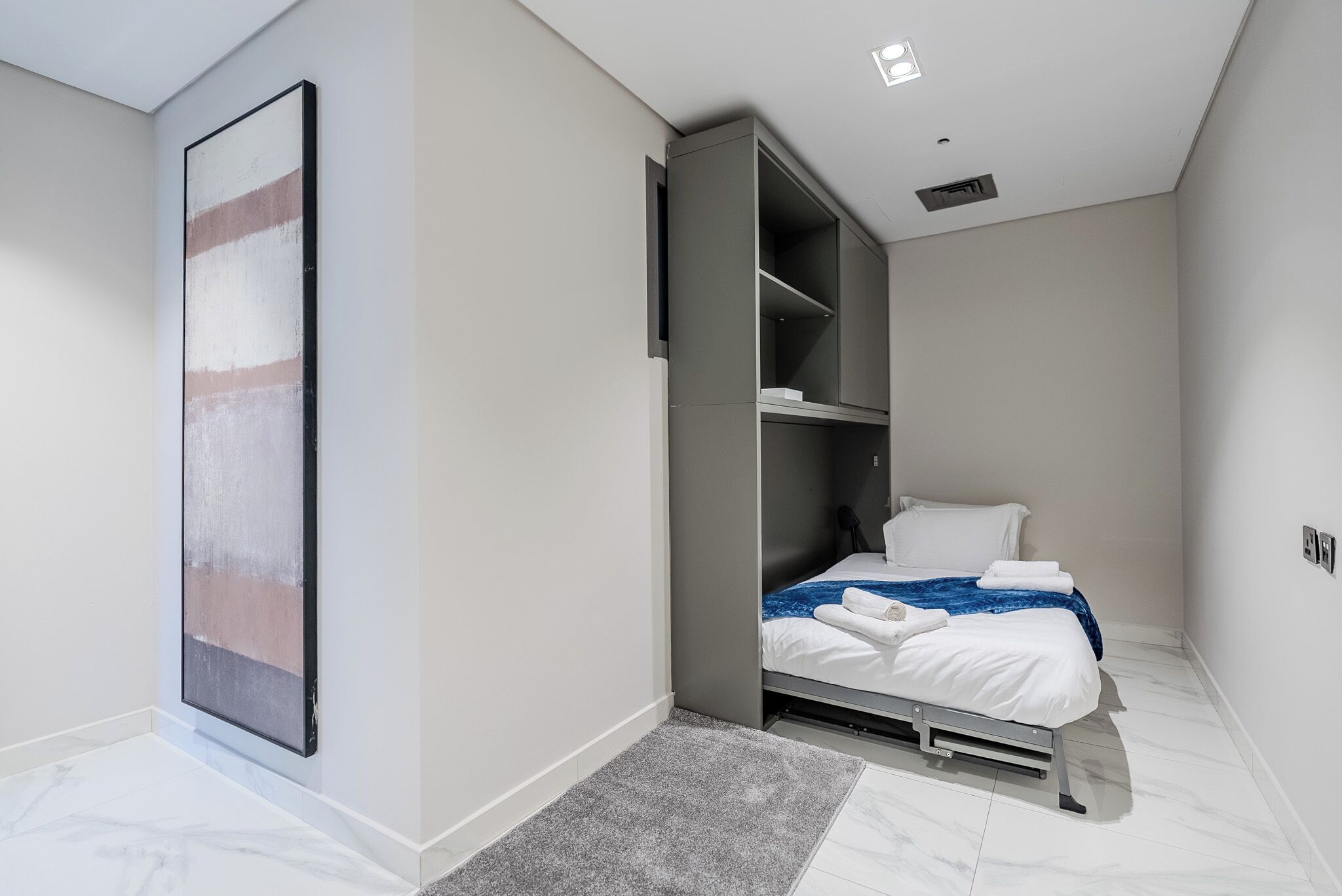 A modern bedroom with a bed, built-in wardrobe, and a large abstract painting.