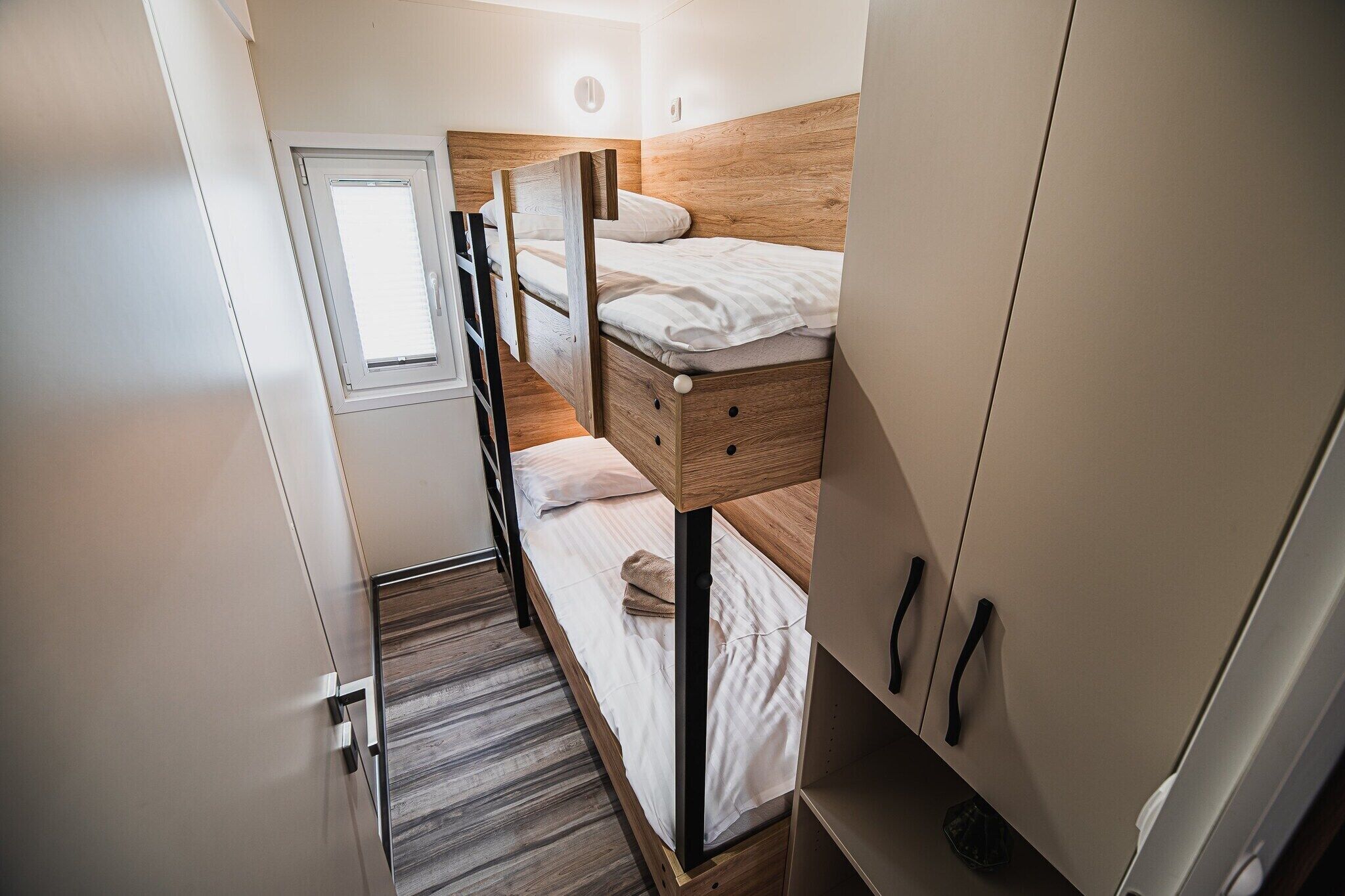 Ein kleines Zimmer mit Etagenbett, kleinem Fenster und Kleiderschrank.