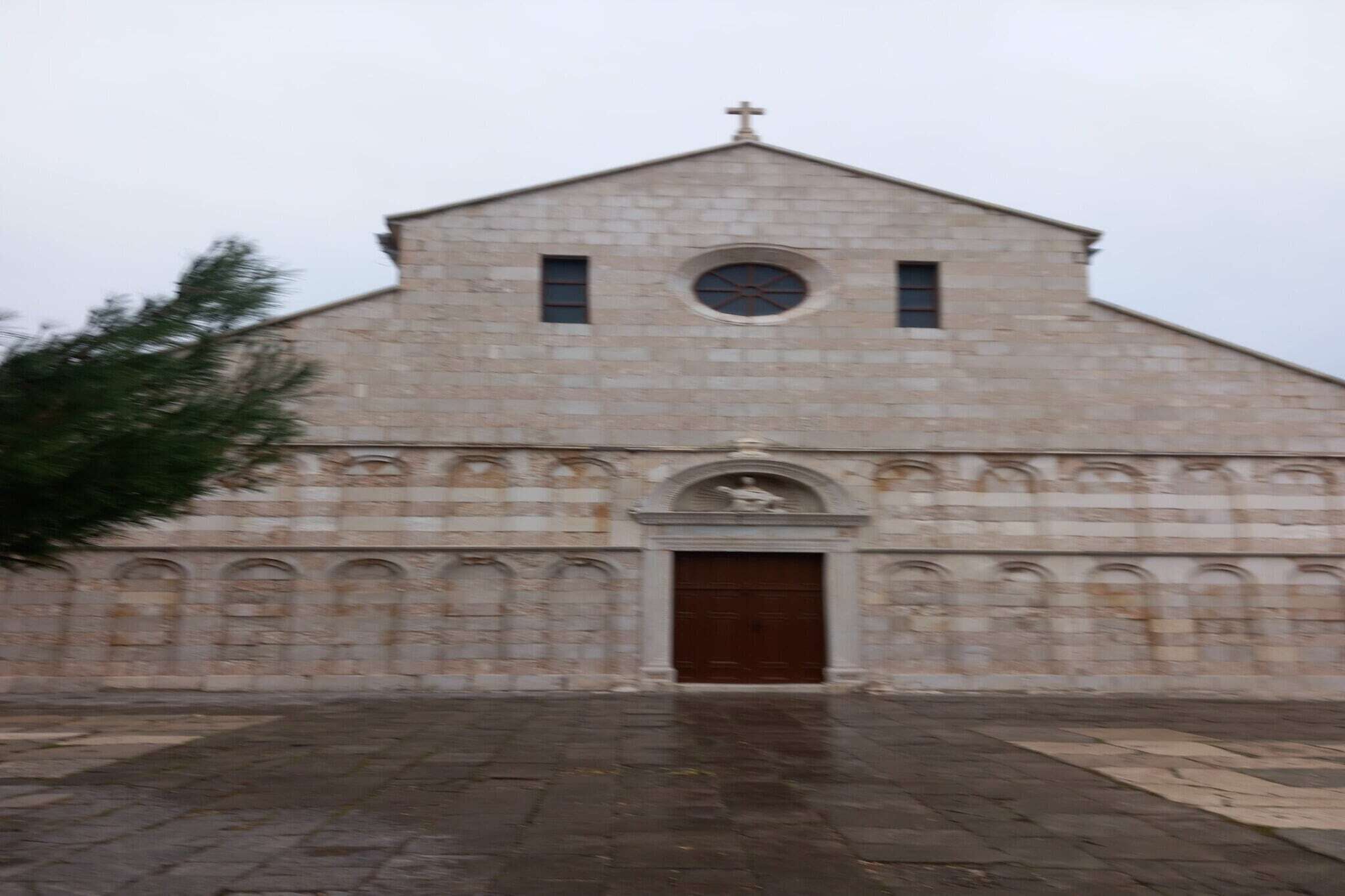 A stone church with a central dome, a cross at the top, and a large wooden door.