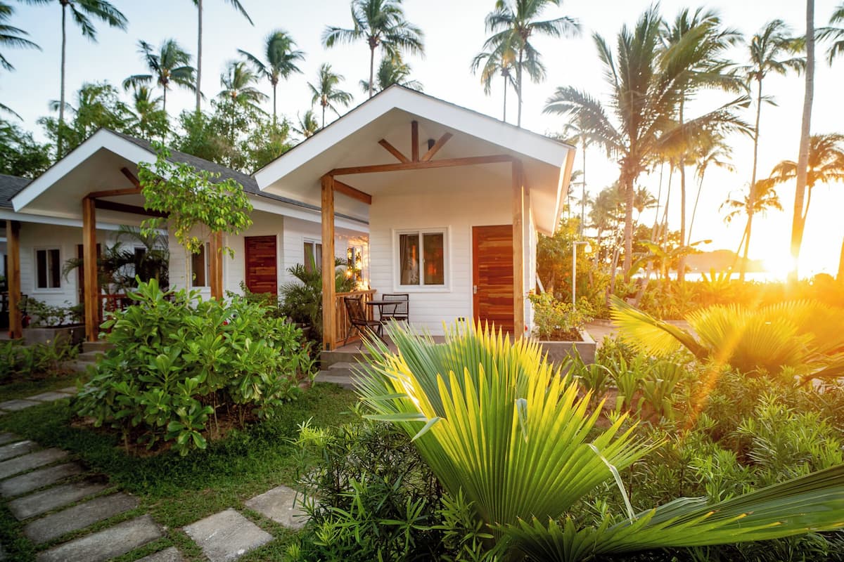 Un hôtel de style bungalow doté d’une véranda couverte, de palmiers et d’un jardin.
