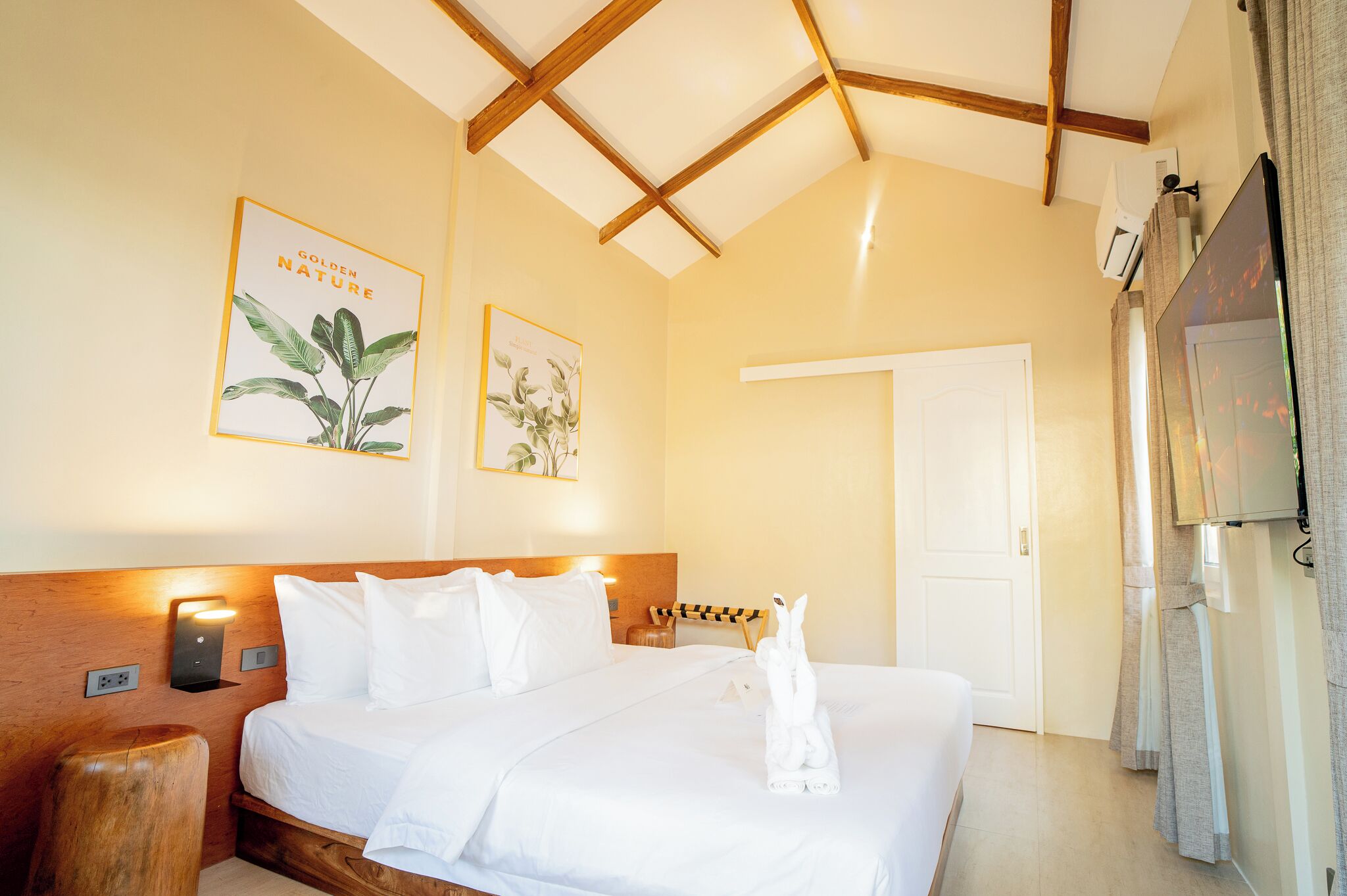 A hotel room with a wooden headboard, a bed with white linens, two wall-mounted light fixtures, and a framed botanical print.