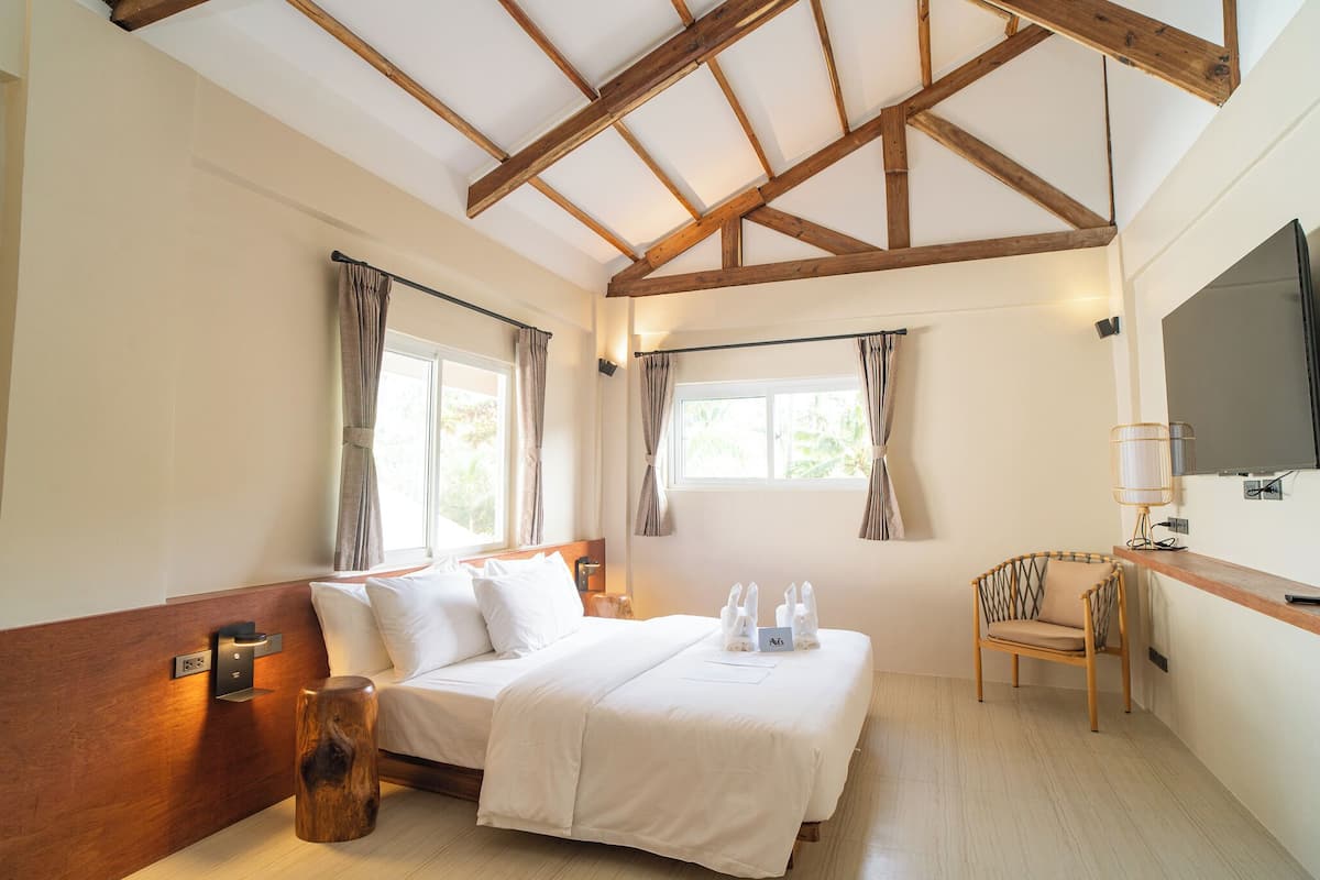 Une chambre à coucher avec une tête de lit en bois, un lit recouvert de draps blancs, une table de chevet avec une lampe et une chaise.
