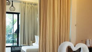 Ein Hotelzimmer mit Bett, Vorhängen, einer Glastür, die nach draußen führt, und zwei Pendelleuchten.