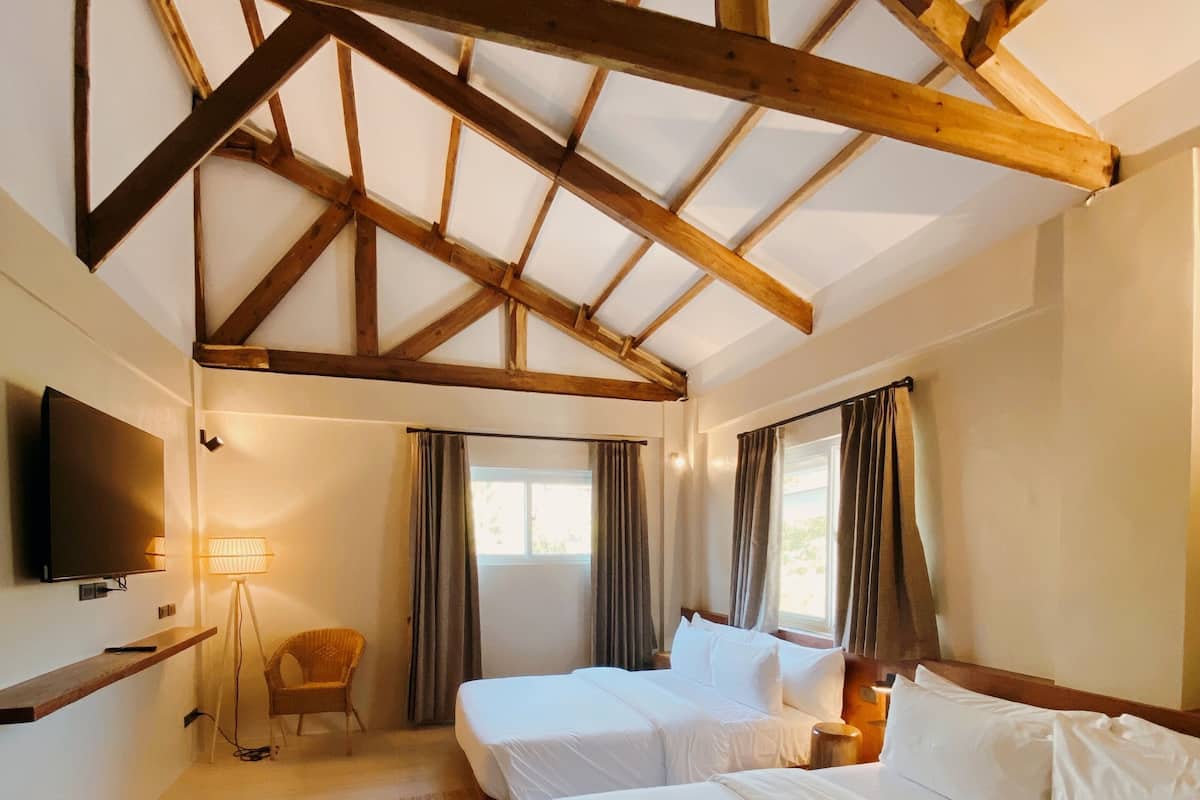 Une chambre d’hôtel avec un plafond en bois, deux lits, une télévision, une chaise et un tapis.