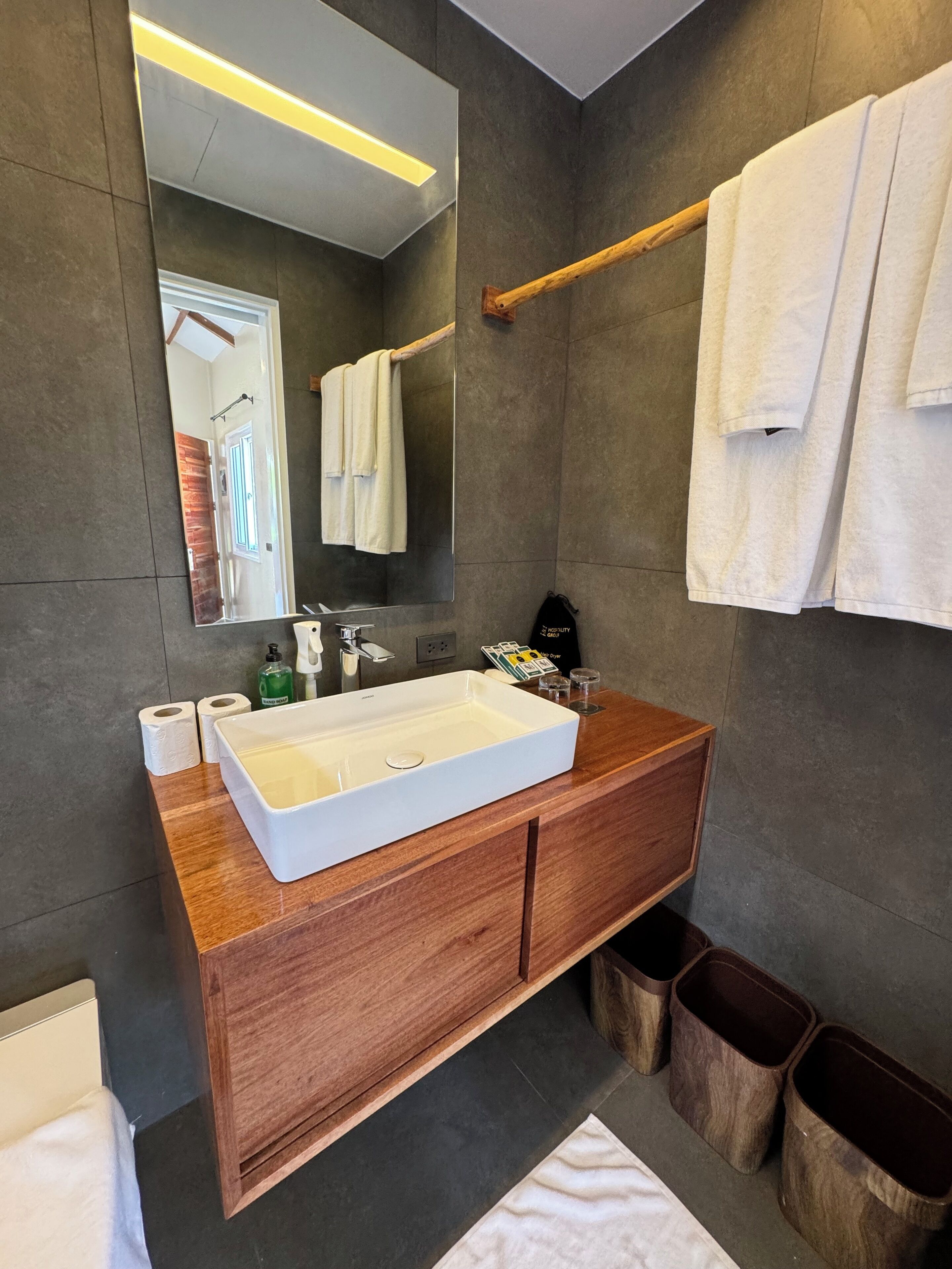 A modern bathroom with a large mirror, wooden vanity, white sink, and multiple towels.