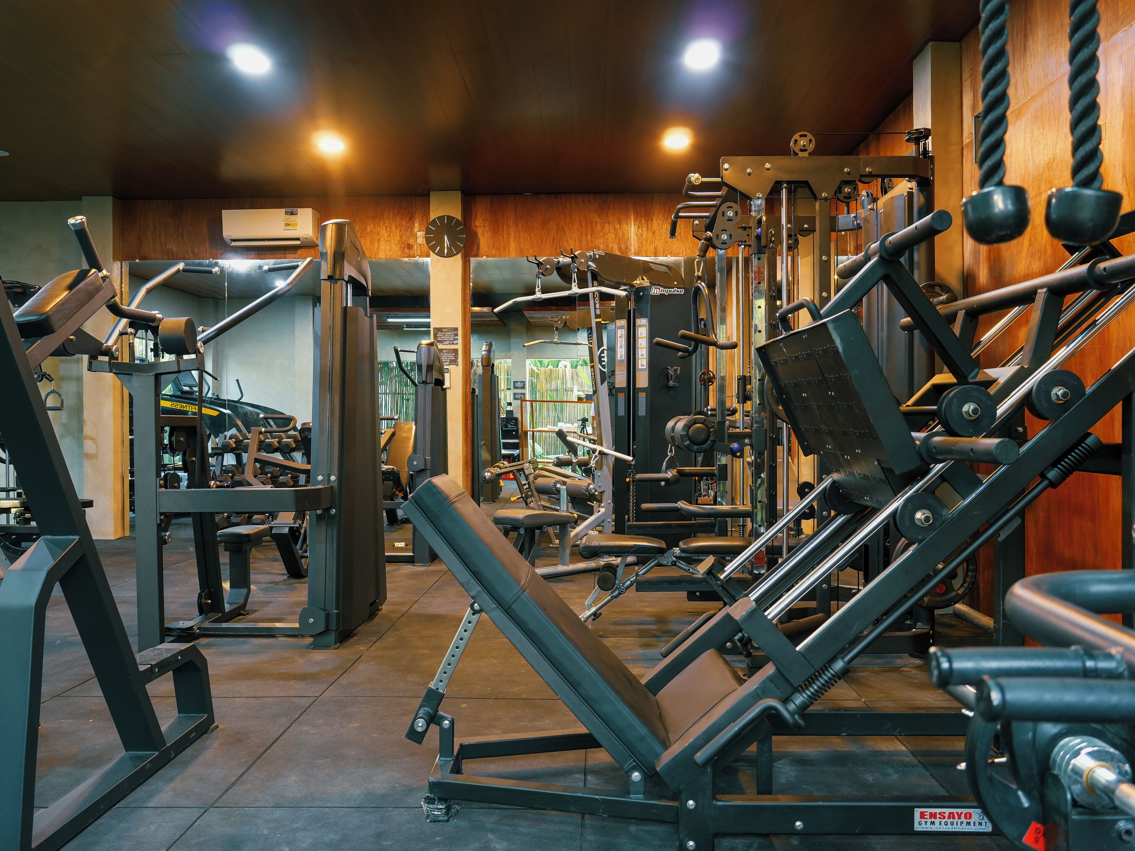 A gym with various exercise equipment, wooden walls, and a clock on the wall.