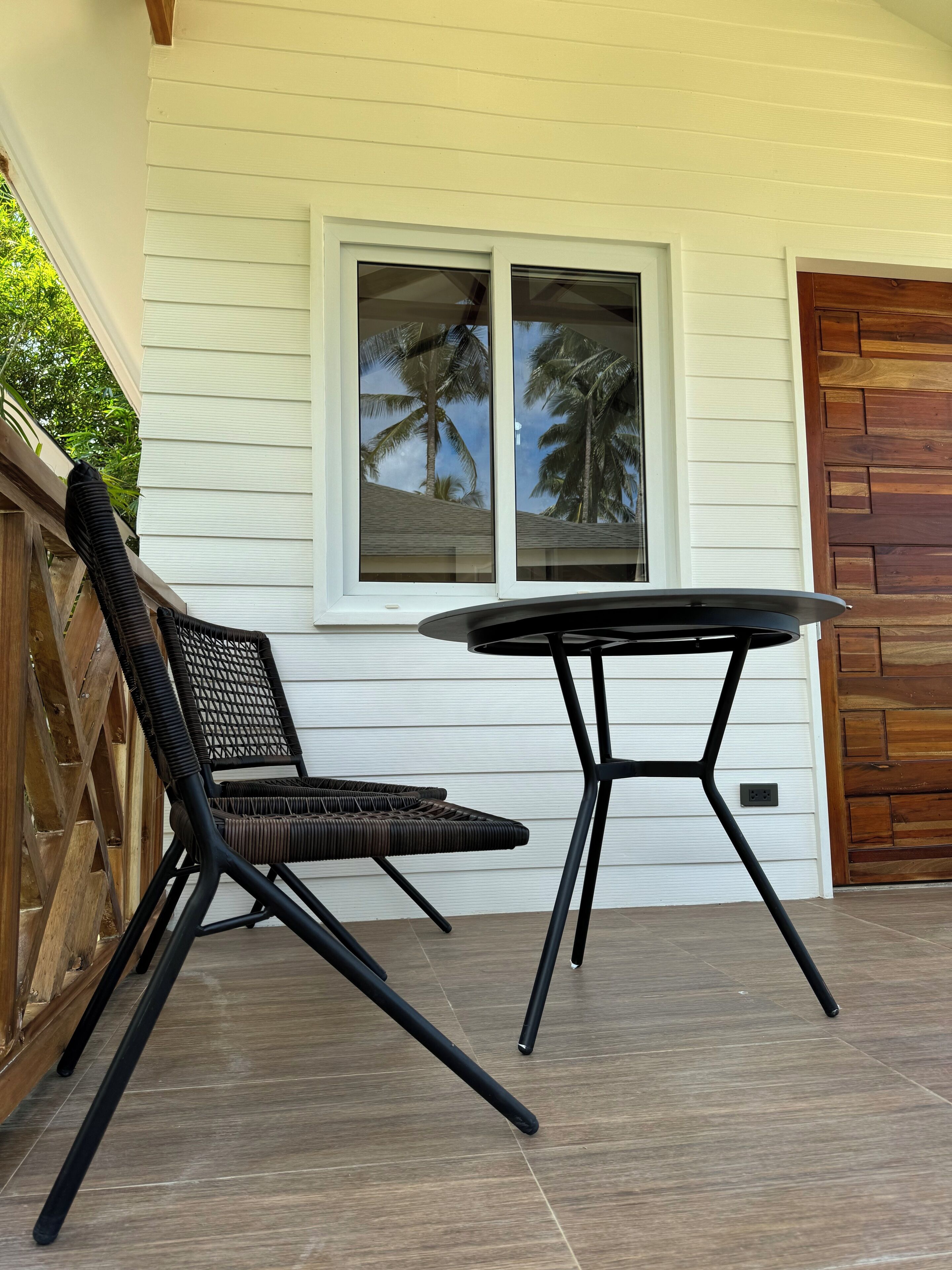 A patio with a table and chairs, a window with a view of palm trees, and a wooden door.