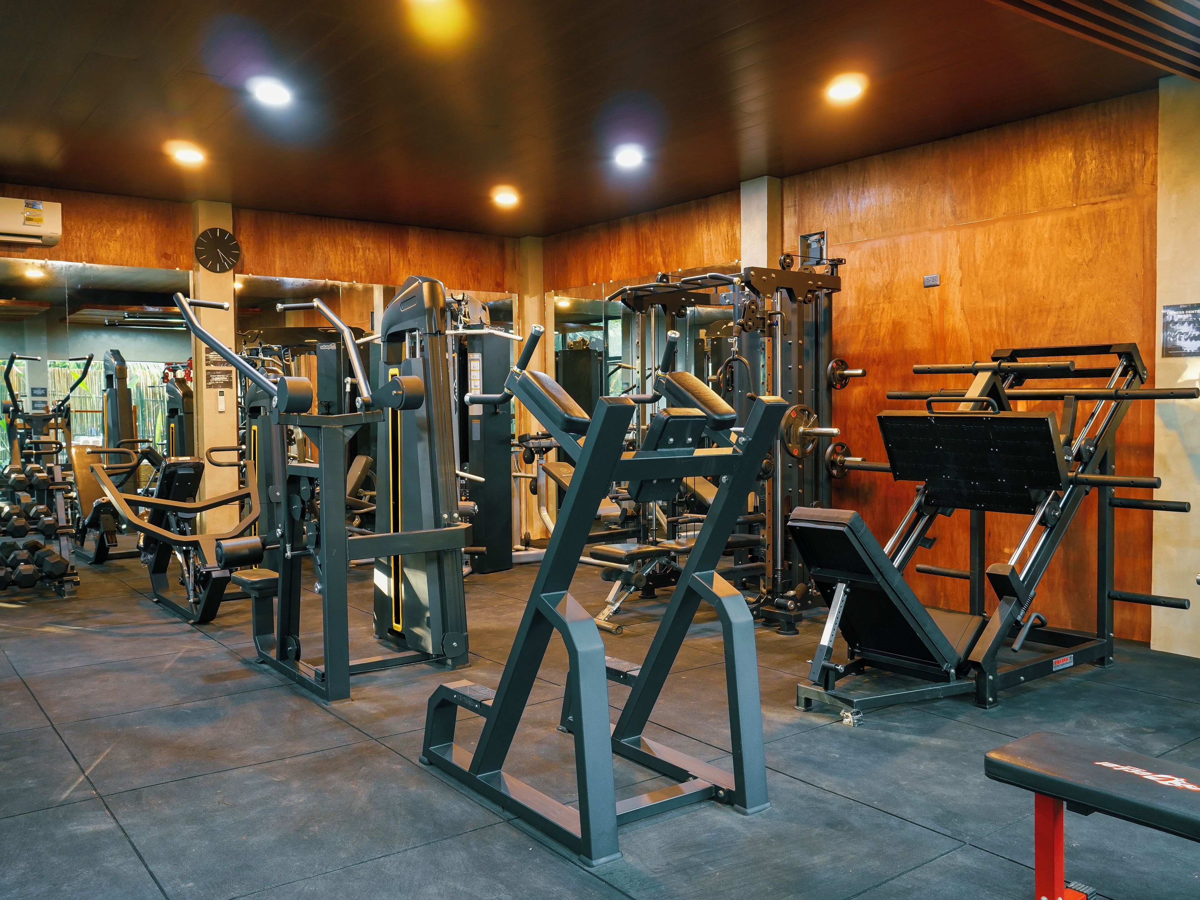 Une salle de sport équipée de divers appareils d’exercice, avec une horloge et un mur en bois.