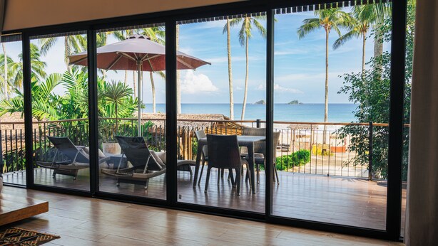 Ein Zimmer mit einer großen Schiebeglastür, die auf einen Balkon mit Meerblick, Sitzmöbel und einem Tisch führt.