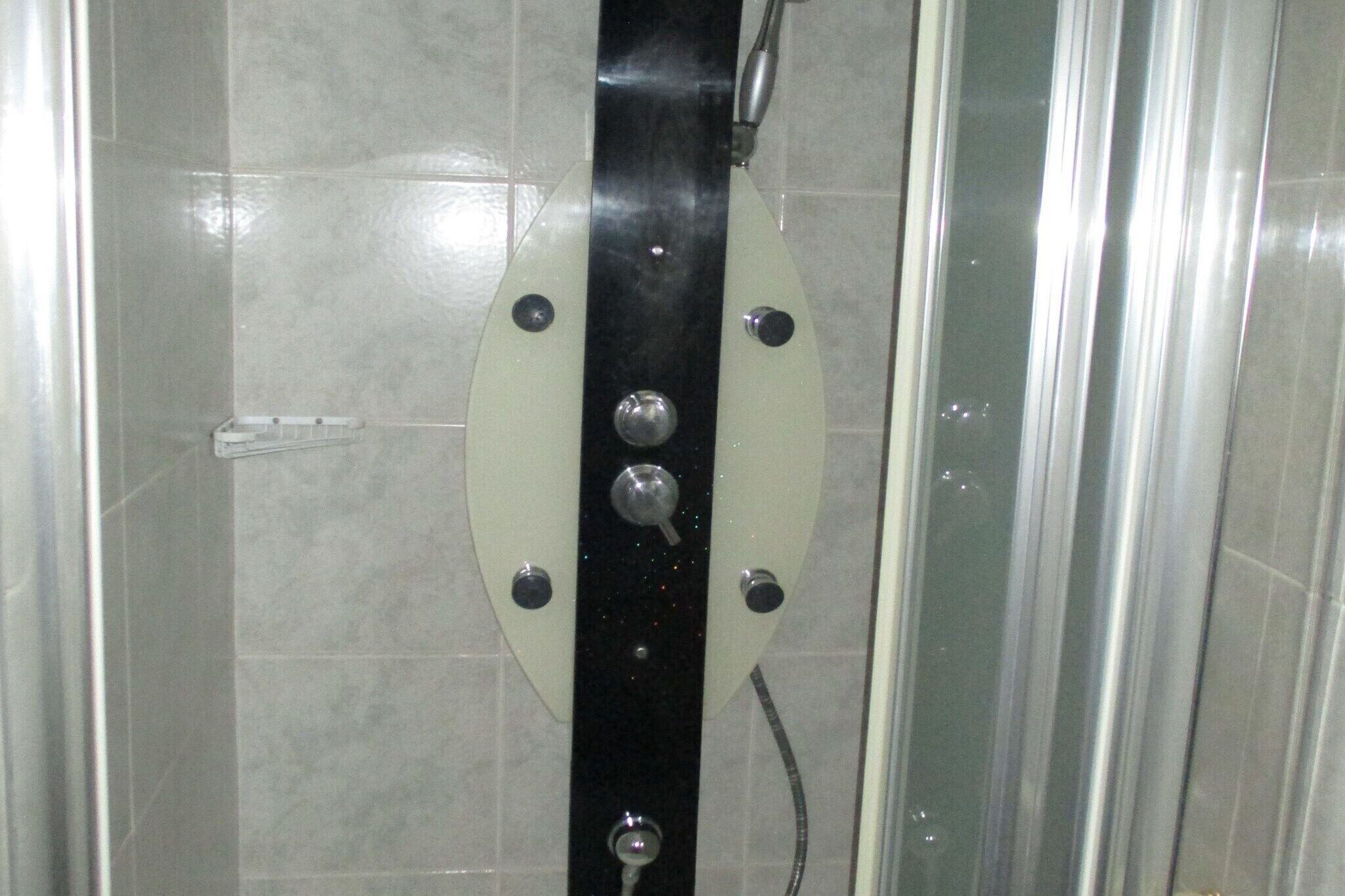 Un box de ducha con puerta de cristal, panel de control con varias perillas y pared de azulejos.