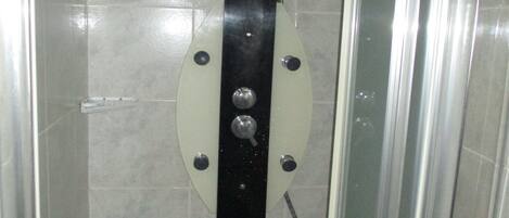 Un box de ducha con puerta de cristal, panel de control con varias perillas y pared de azulejos.