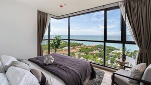 Une chambre moderne dotée d’une grande fenêtre offrant une vue sur la mer et le paysage urbain.