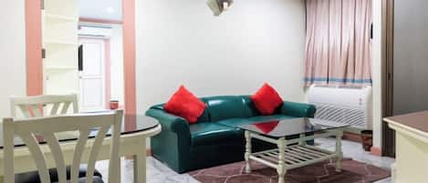 Una sala de estar con un sofá verde, cojines rojos, una mesa de centro blanca y un suelo de mármol.