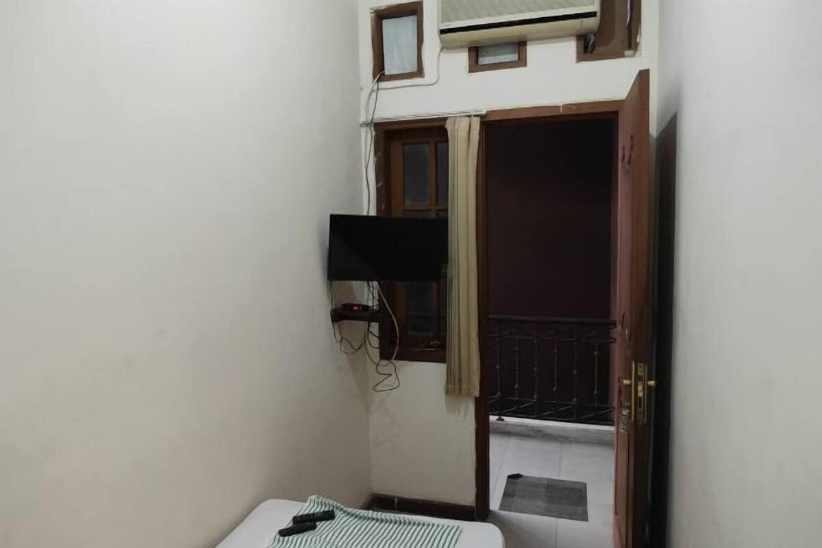 A small room with a bed, a TV mounted on the wall, a window with curtains, and a door leading to a balcony.